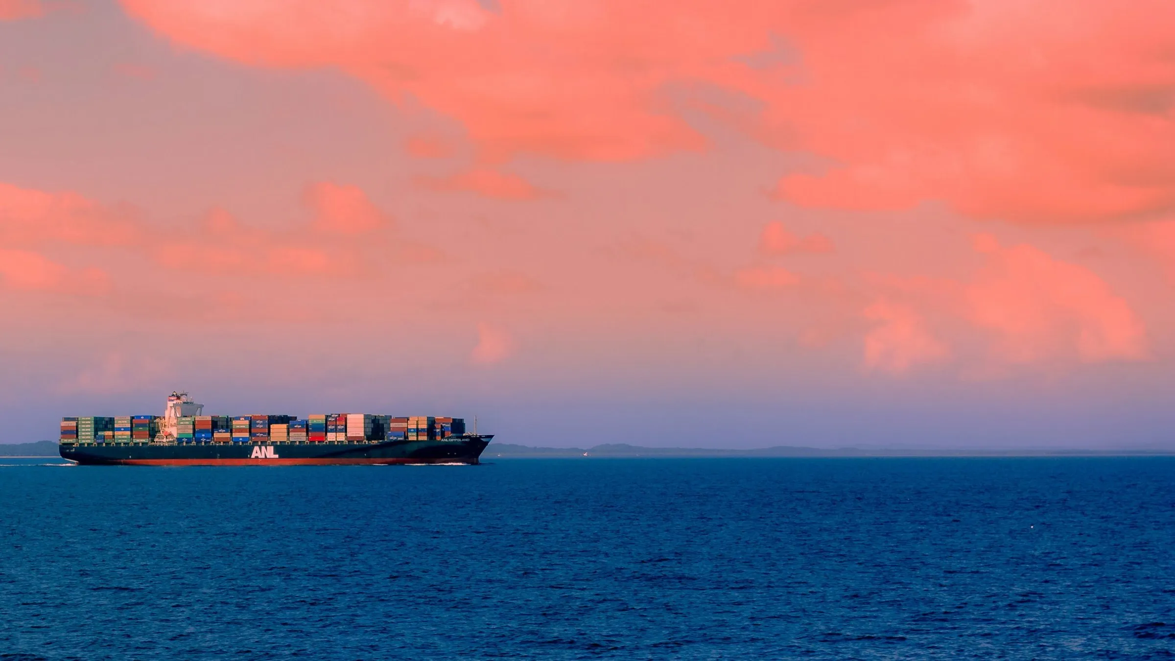 A container ship crossing open water under a pink sunset sky