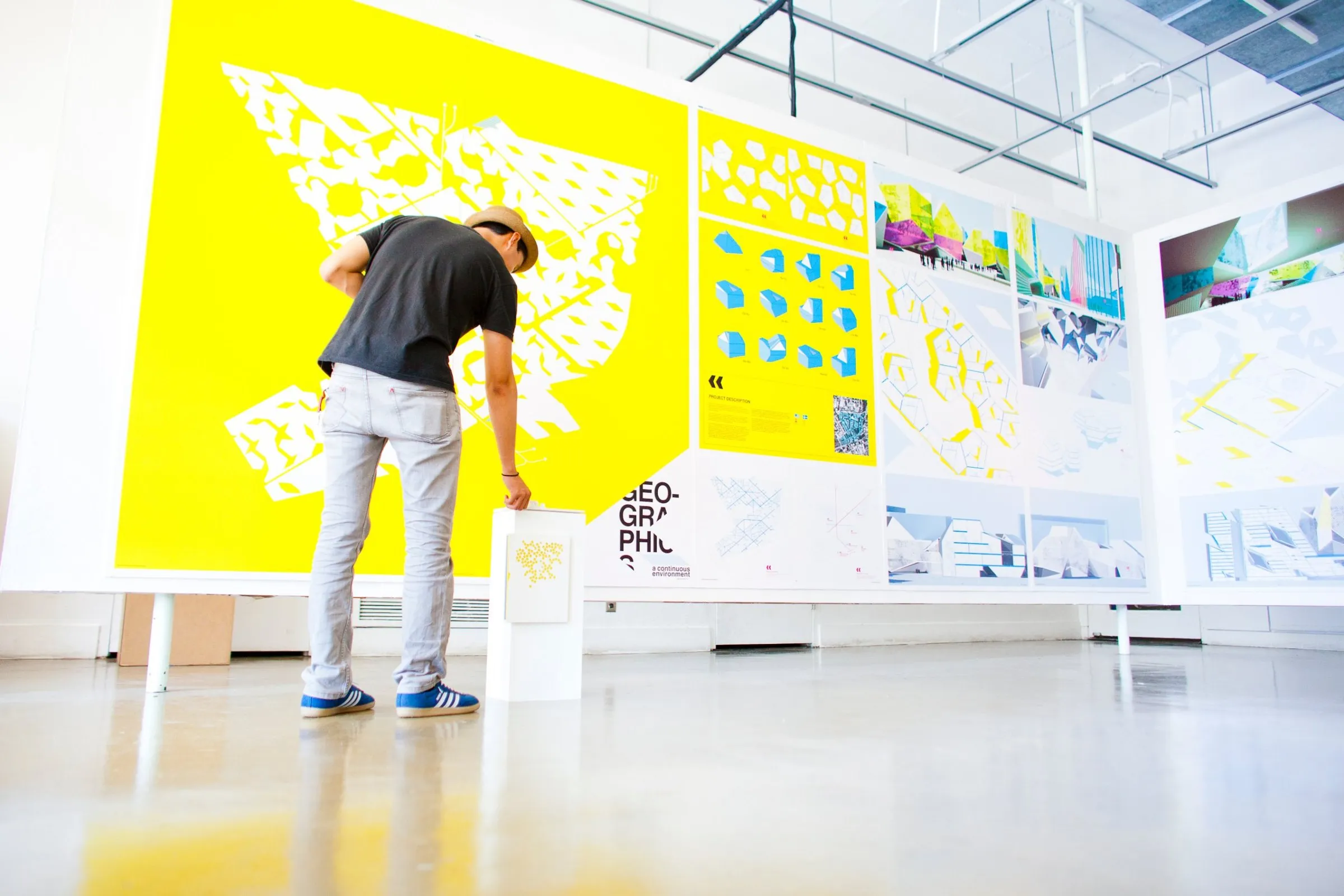 A student studying a large yellow architecture exhibition wall in a bright gallery